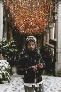 Portrait of man standing in snow against illuminated lighting equipment outdoors