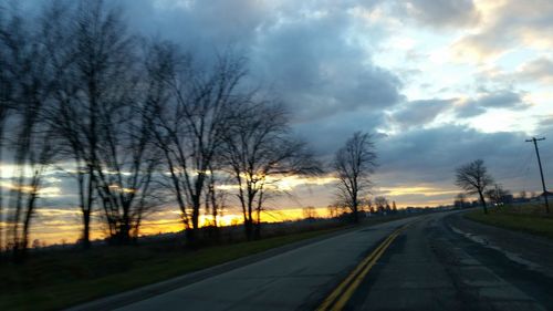 Road by bare trees against sky during sunset