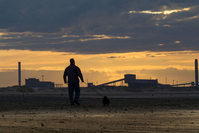 Silhouette man standing at beach against cloudy sky during sunset