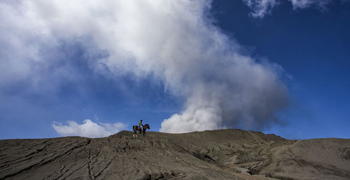 Mid distance view of person riding horse at mt bromo against blue sky