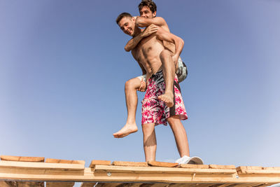 Low angle view of friends standing against clear blue sky