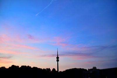 Silhouette of communications tower in city against sky during sunset