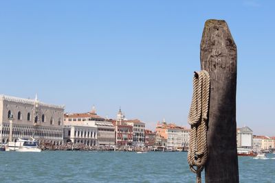 Rope on wooden pole at river by buildings against clear sky