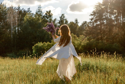 Young beautiful woman, wearing white dress, holding flowers and dancing on the meadow. girl joying