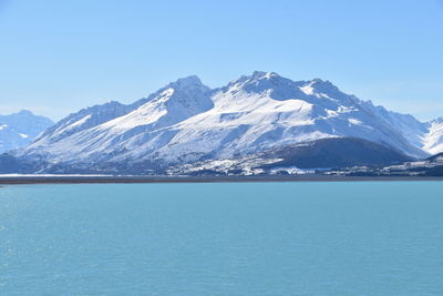 Scenic view of sea and snowcapped mountain against blue sky