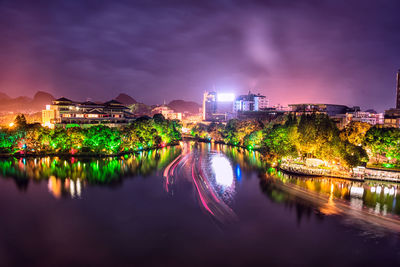 Illuminated buildings by river against sky at night