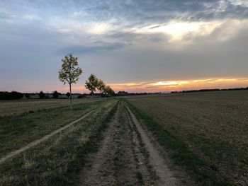 Road amidst field against sky during sunset