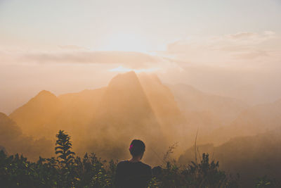 Rear view of man looking at mountains during sunset