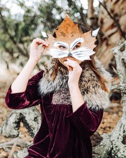 Portrait of girl holding maple leaf while standing in park during autumn