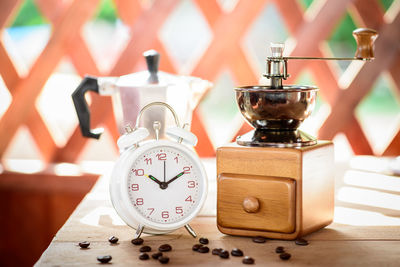 Close-up of coffee grinder with alarm clock on wooden table