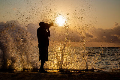 Rear view of silhouette woman standing against lake during sunset