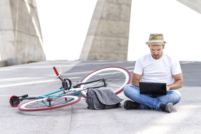 Man using laptop while sitting by bicycle on street
