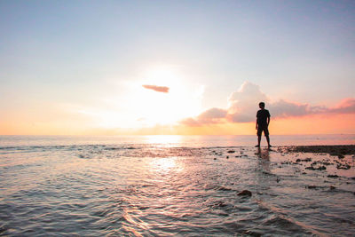 Silhouette man standing on beach against sky during sunset