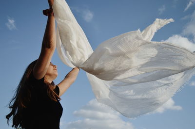 Low angle view of woman holding scarf while standing against sky