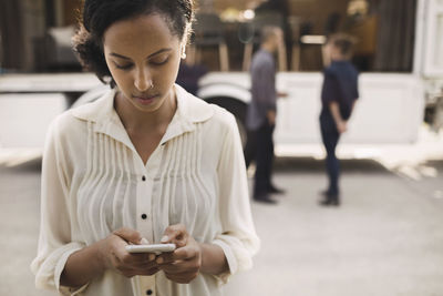 Businesswoman using smart phone with colleagues and portable office truck on road in background