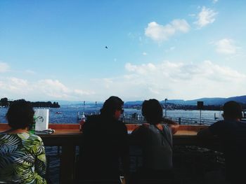 Rear view of people sitting at beach against sky