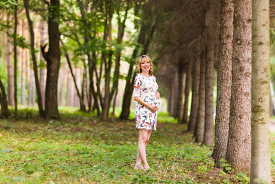 Full length of boy standing by tree trunk in forest