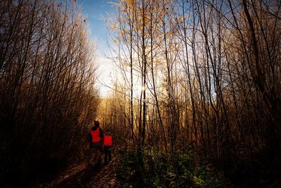 Woman standing by bare trees in forest against sky