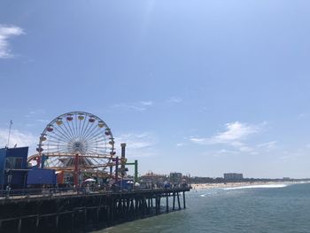 Ferris wheel by sea against sky in city
