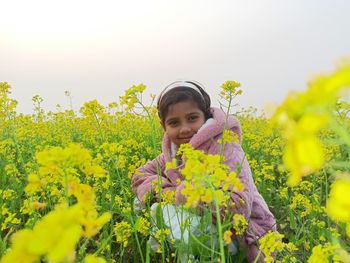 Portrait of smiling young woman standing amidst yellow flowering plants against sky