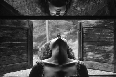 Young woman peeking through window reflecting on mirror