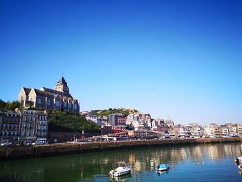 Boats in river by buildings against clear blue sky