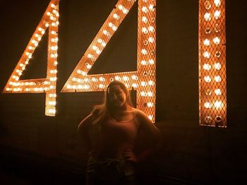 Full length of woman standing against illuminated light at night