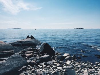 People on rocks by sea against sky