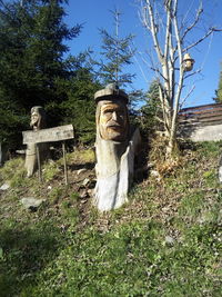 Statues on field by trees against sky