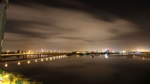 Illuminated city by river against sky at night