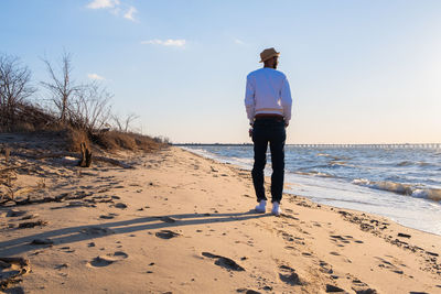 Rear view of man standing on beach against sky