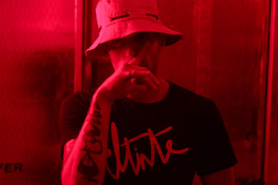 Young man wearing hat standing against red wall