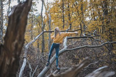 Full length of girl standing on tree trunk in forest