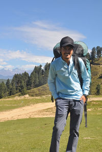 Front view of a happy young guy wearing cap with carrying parachute backpack in the mountain 