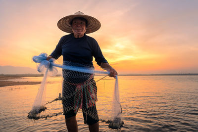 Fisherman holding fishing net while standing in lake against sky