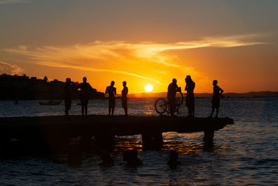 Young people, in silhouette, are seen together, enjoying the sunset from the top of the crush bridge