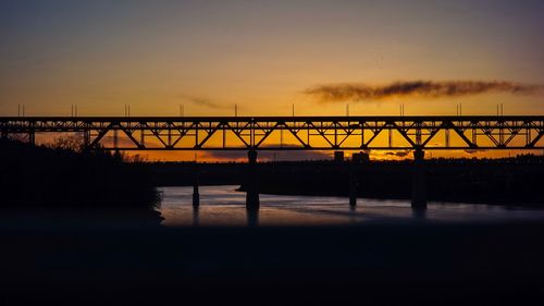 Silhouette bridge over river against sky during sunset