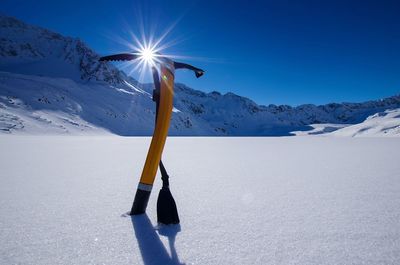 Ice axe on snow covered field against clear blue sky