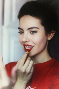 Smiling young woman applying red lipstick