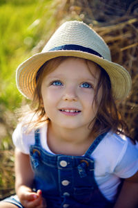 Little girl in the haystack in a hat and denim overalls