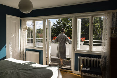 Rear view of woman opening doors of bedroom while walking in balcony