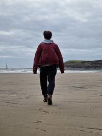 Rear view of woman walking on beach against sky