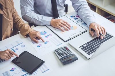 Midsection of colleagues working over graph at desk in office