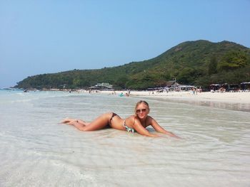 Young woman in bikini swimming at beach against clear sky