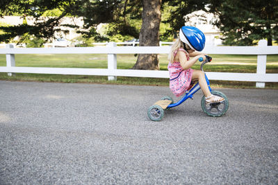 Side view of girl riding tricycle on road wearing helmet