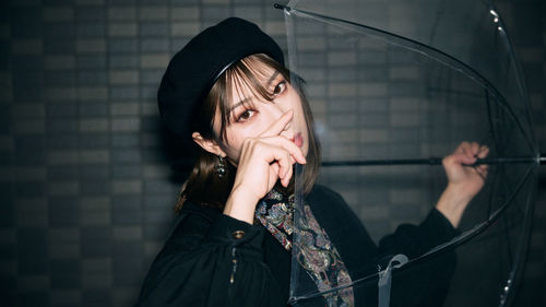 Portrait of young woman holding hat against wall