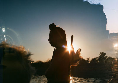 Silhouette people in water against sky at sunset