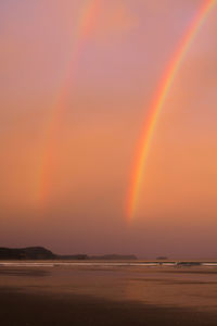 Scenic view of rainbow over sea against sky during sunset