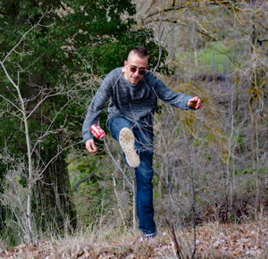 Young man kicking beer can in forest