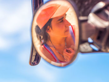Reflection of young woman on bicycle side-view mirror against sky